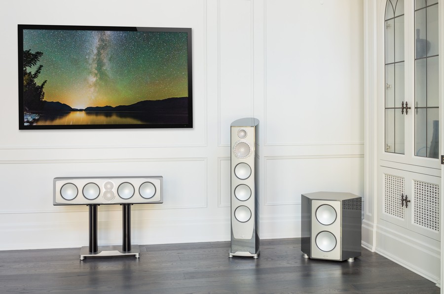 Three paradigm speakers situated beneath a TV in a white room.