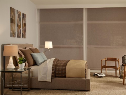 a bedroom with closed motorized shades and a bed with tan and brown comforter and brown and silver pillows. 
