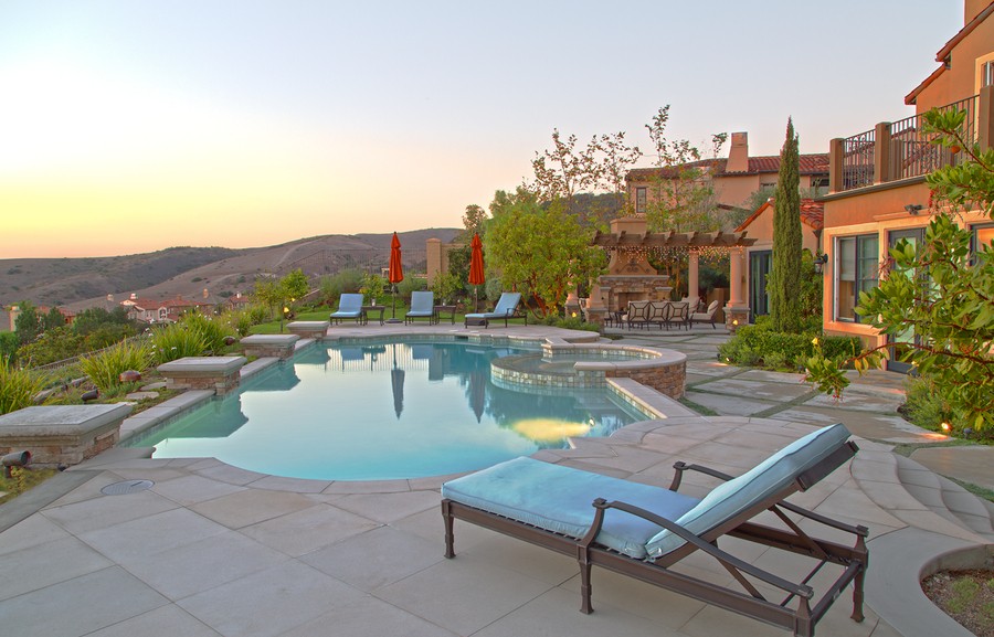 A backyard with a pool, fireplace, and Sonance speakers installed along the perimeter.