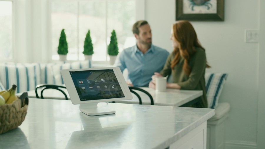 A man and woman sitting at the kitchen counter of their home, a Control4 control panel at the forefront.