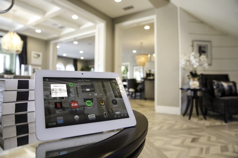 A Control4 control touchscreen on a table in a luxury home streaming a song on Spotify.