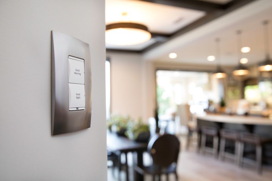 A Control4 lighting keypad with a brightly lit home in the background.