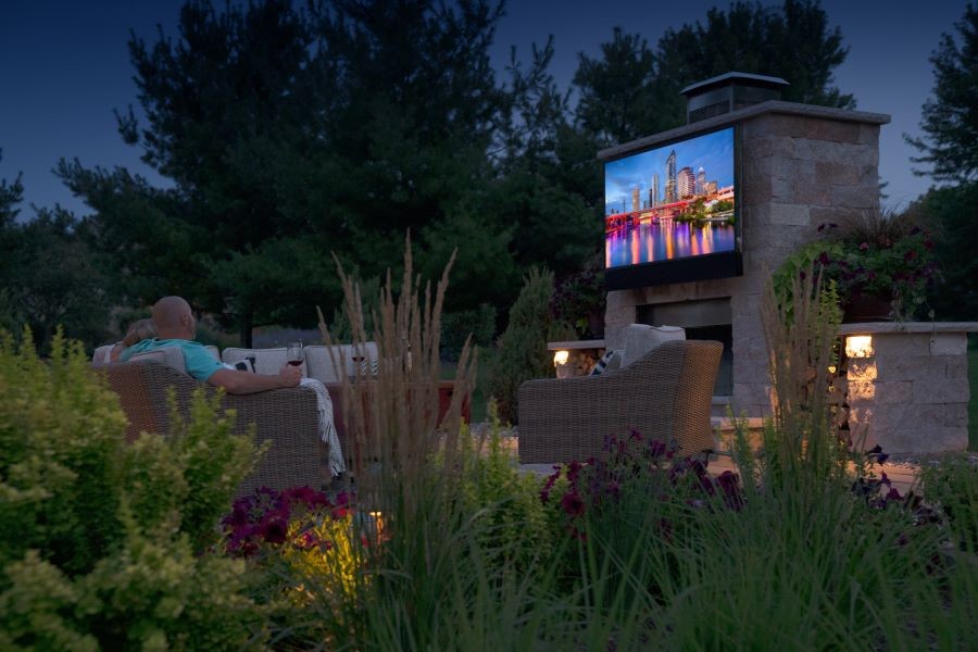 People watching an outdoor TV amidst beautiful landscaping and lighting. 