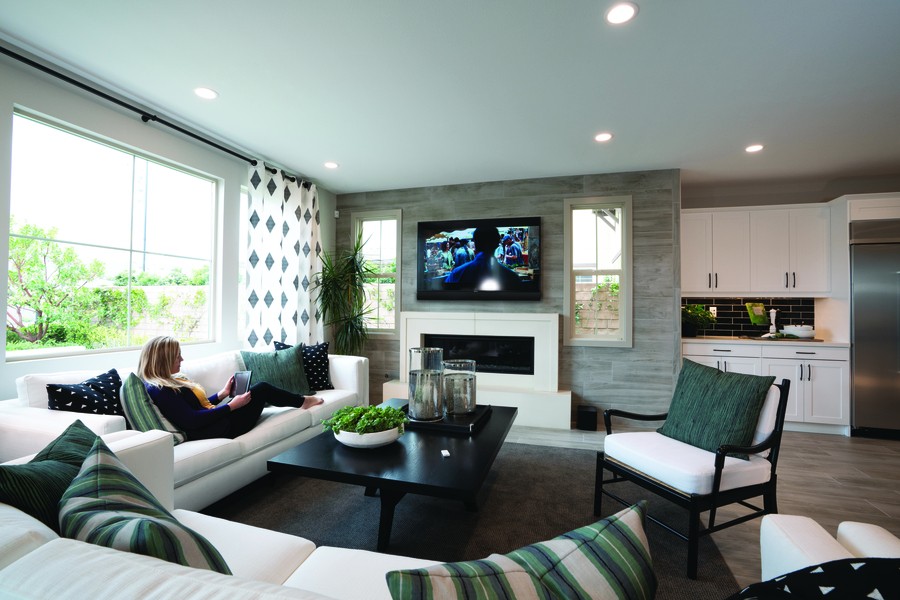 A woman comfortably watching a wall-mounted TV on a couch in a family room. 