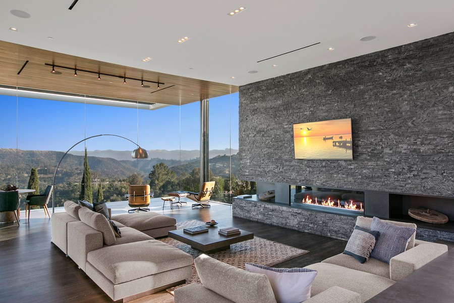 A modern home with floor-to-ceiling windows, in-ceiling speakers, and a TV above a fireplace. 