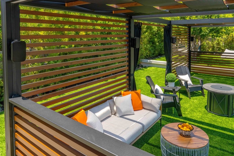 A patio space with a pergola, a seating area on the grass, and outdoor speakers mounted on the pergola posts.