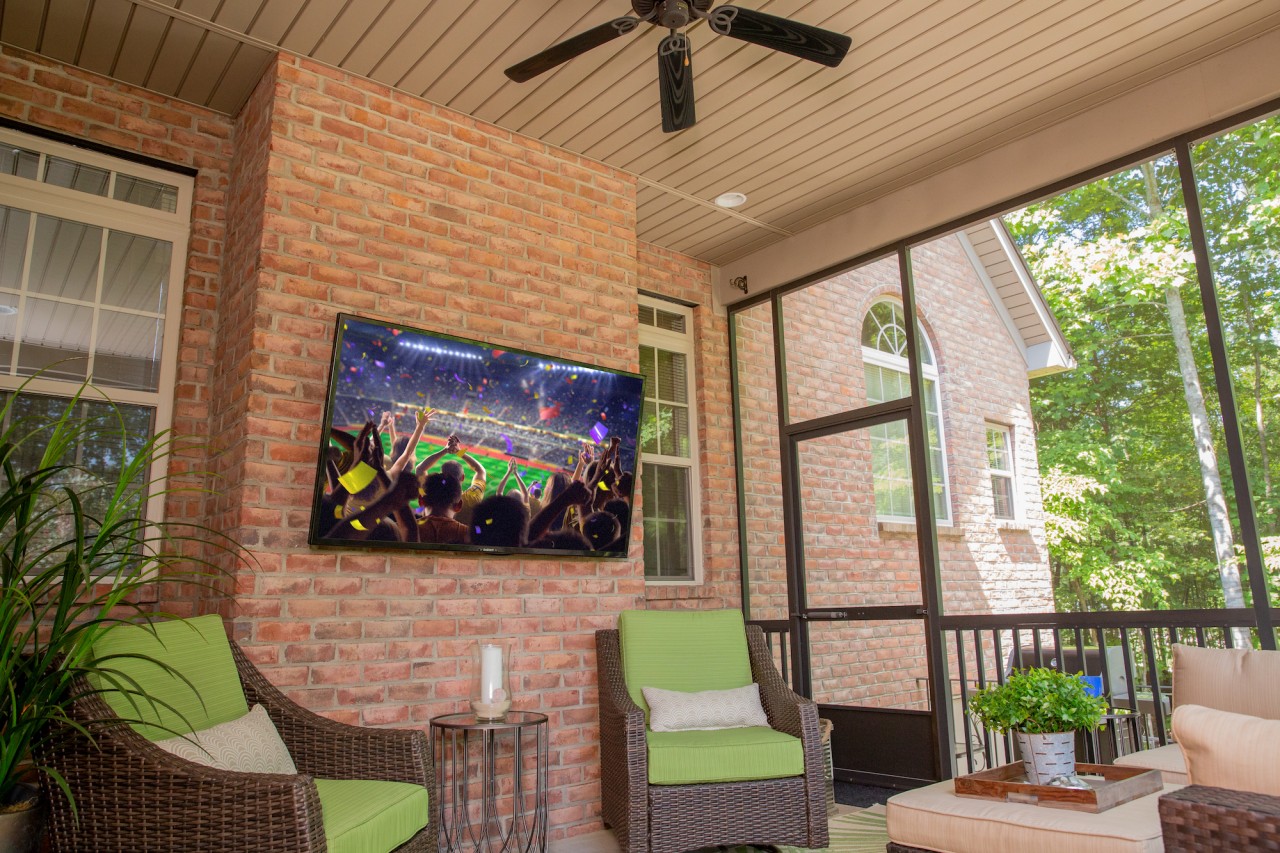 A screened outdoor room attached to a brick home with an outdoor TV for entertainment.